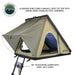 Image displaying an olive green Overland Vehicle Systems roof top tent, fully deployed on top of a white SUV against a desert landscape, ready for outdoor adventure. The tent has a "TMON" logo on its side