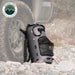 Image of Overland Vehicle Systems portable camp shower bag standing upright next to an off-road vehicle tire, gray waterproof design with mesh pocket and straps shown in outdoor rocky terrain setting