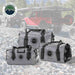 Image of three gray Overland Vehicle Systems IPX6 waterproof duffel bags (69, 42, and 58 Quart) on a rocky terrain background with an overland vehicle and tent in the soft-focus distance.