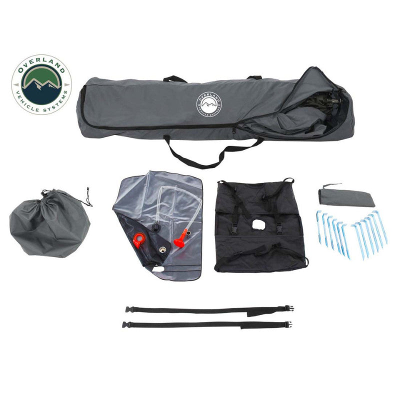 Image of a portable privacy shower tent kit showing carry bag, folded tent, ground stakes, straps, and accessories neatly laid out, top-down view on white background.