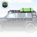 Image of a black roof rack on a Ford Bronco, with a green recovery ramp mounted on top, highlighting that it can easily mount a variety of accessories like tents, awnings, and water cans