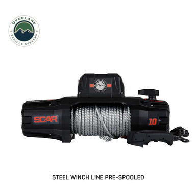 A frontal view of the black and orange Overland Vehicle Systems (OVS) SCAR Series Winch on a white background. The winch is shown with a pre-spooled steel winch line, with the wired remote control placed next to it