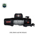 A frontal view of the black and orange Overland Vehicle Systems (OVS) SCAR Series Winch on a white background. The winch is shown with a pre-spooled steel winch line, with the wired remote control placed next to it