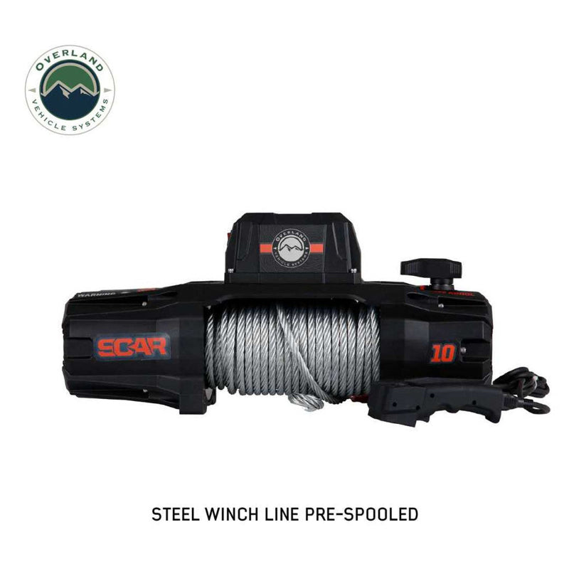 A frontal view of the black and orange Overland Vehicle Systems (OVS) SCAR Series Winch on a white background. The winch is shown with a pre-spooled steel winch line, with the wired remote control placed next to it