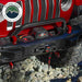 Image of an Overland Vehicle Systems (OVS) SCAR winch installed on the front bumper of a red Jeep Wrangler, with a hook connected to a winch line. The vehicle is on a rocky, off-road surface