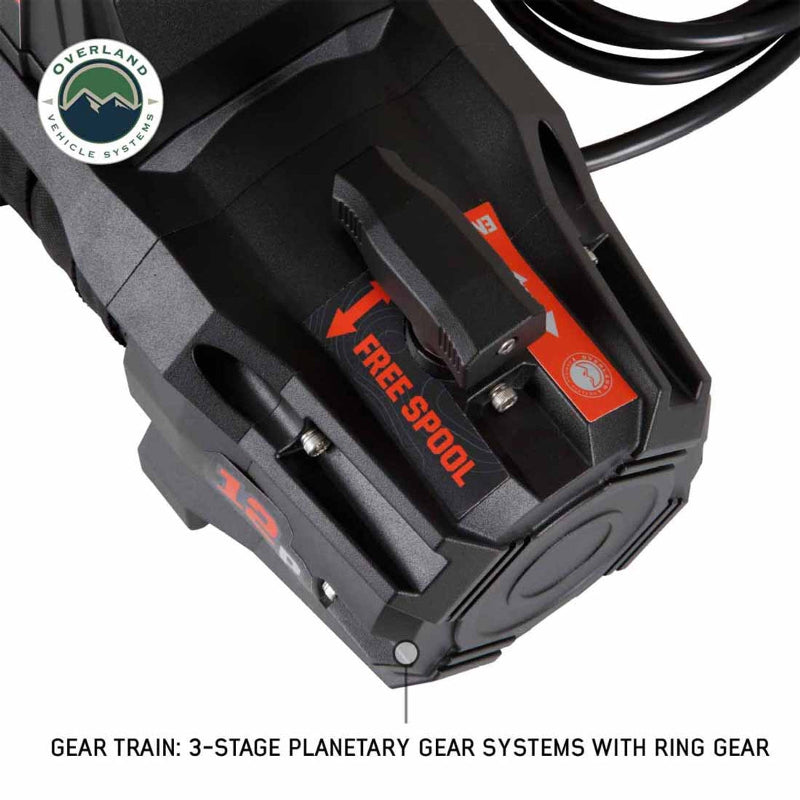 Image of the side of the Overland Vehicle Systems (OVS) SCAR winch, highlighting the 'FREE SPOOL' lever and the 12,000 lb. rating in red text. An inset text box describes the "3-STAGE PLANETARY GEAR SYSTEMS WITH RING GEAR"