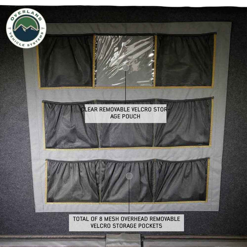 Image showing the interior ceiling of a rooftop tent, featuring a total of 8 mesh overhead removable velcro storage pockets, including one clear removable velcro storage pouch, all against a dark grey fabric background. The "Overland Vehicle Systems" logo is in the top left corner