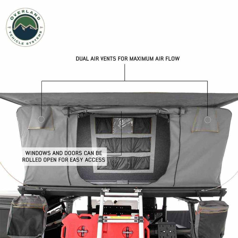 Image showcasing the interior features of a dark grey rooftop tent, highlighting dual air vents for maximum airflow and windows/doors that can be rolled open for easy access. Camping gear like a red fuel can and ladder are visible below the tent, with the "Overland Vehicle Systems" logo in the top left, all on a white background