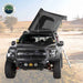 Image of a black Ford pickup truck with a dark grey hardshell rooftop tent partially deployed on its roof, positioned in a desert landscape with a ladder extended to the side. The truck features aftermarket off-road lights and a rugged front bumper, with the "Overland Vehicle Systems" logo in the top left