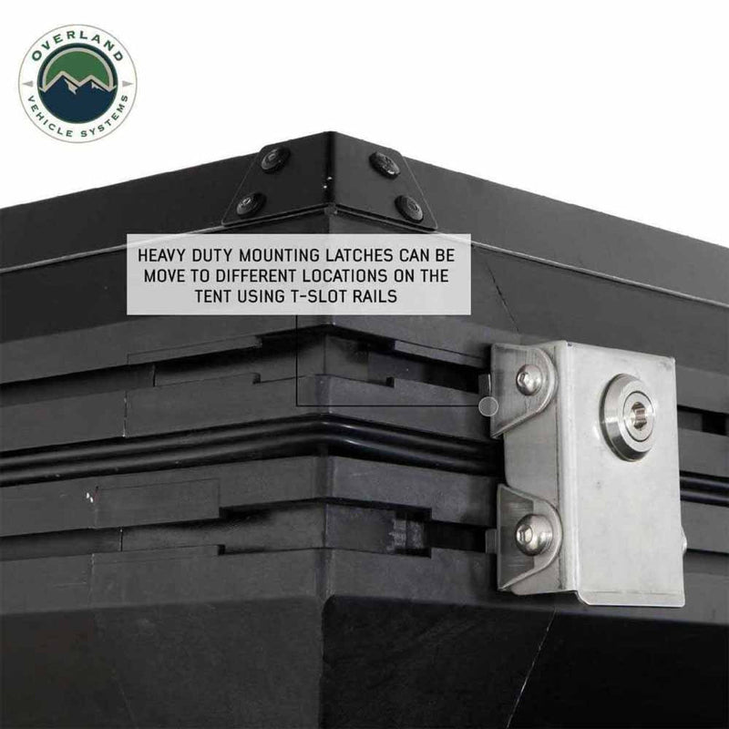 Image close-up of a black hardshell rooftop tent, highlighting its heavy-duty mounting latches that can be moved using T-slot rails, with a silver latch mechanism visible on the side. The "Overland Vehicle Systems" logo is in the top left corner, all on a white background
