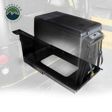 Image of portable electric refrigerator mounted on a heavy-duty sliding tray, black fridge unit with pull-out steel platform partially extended, angled front and side view on white background.