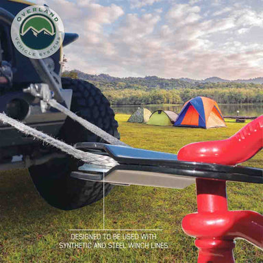 Image of Overland Vehicle Systems standard snatch block in use with synthetic winch line on an off-road vehicle, black recovery pulley guiding cable near campsite setting, angled side view in outdoor terrain.