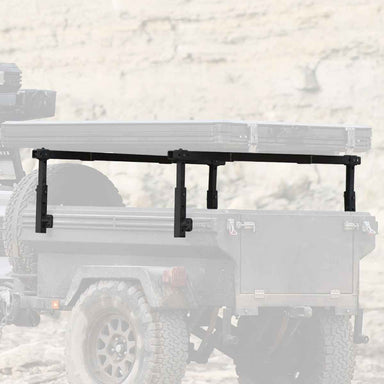 Image of a black OVS Overland Vehicle Systems Freedom Rack cargo carrier mounted on the back of an off-road trailer, shown against a blurred outdoor background