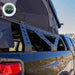 Image of Overland Vehicle Systems mid-height rack on a black pickup truck, with a roof top tent partially deployed, showing the rack's sturdy build and ability to support outdoor gear, with a clear view of the truck's side and rugged desert landscape in the background