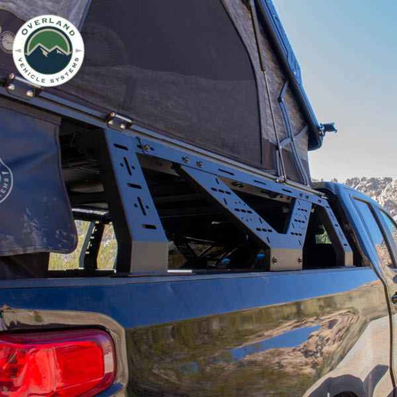 Image of Overland Vehicle Systems mid-height rack on a black pickup truck, with a roof top tent partially deployed, showing the rack's sturdy build and ability to support outdoor gear, with a clear view of the truck's side and rugged desert landscape in the background