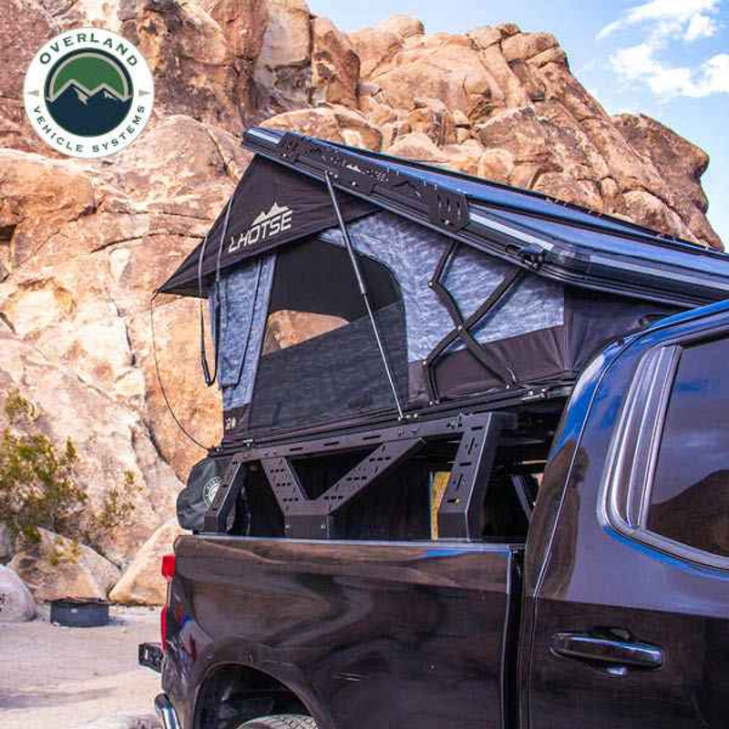 Image of a mid-height rack with a roof top tent fully deployed, set on a black pickup truck, with the rugged desert landscape and rocky terrain in the background, showcasing the sturdy and reliable structure of the rack