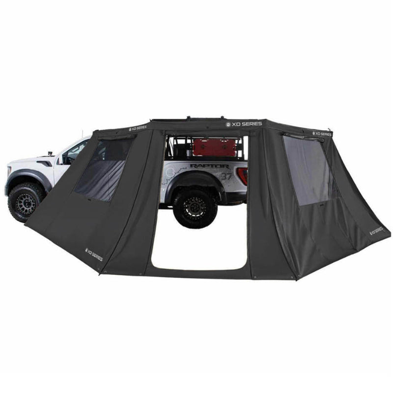 Image of OVS XD Nomadic 180 LTE awning walls fully enclosed around a pickup truck, black fabric with window panels, creating a sheltered camping area shown in side view on a white background.