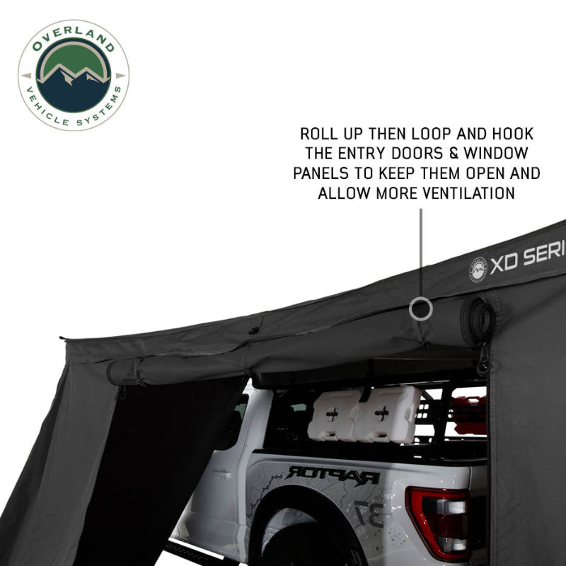 Image of OVS XD Nomadic 180 LTE awning wall with door panel rolled up and secured, black fabric showing hook-and-loop ventilation feature, angled side view on a white background.