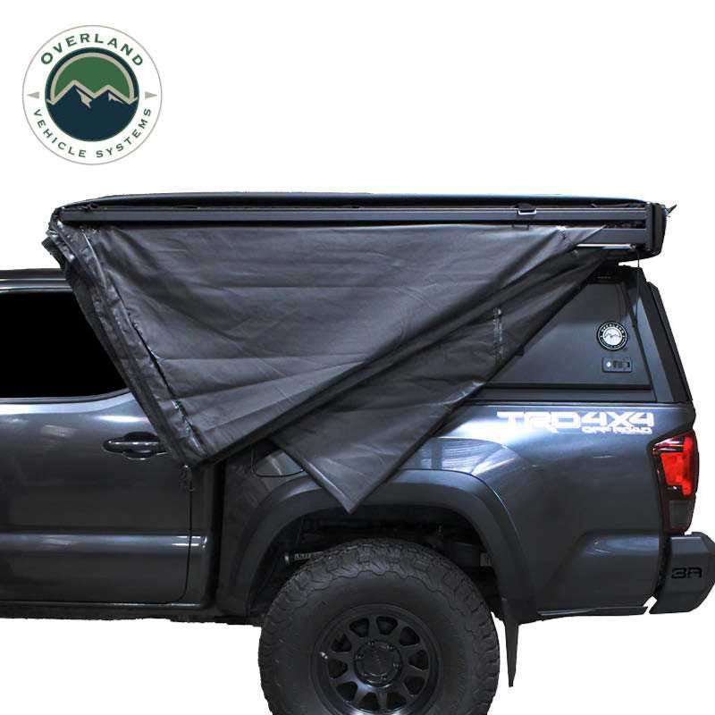 Image showcasing built-in gaze-less and fade-less screen windows on a black Overland Vehicle Systems awning, with a dark interior visible through the mesh. The awning is partially deployed, showing its support structure