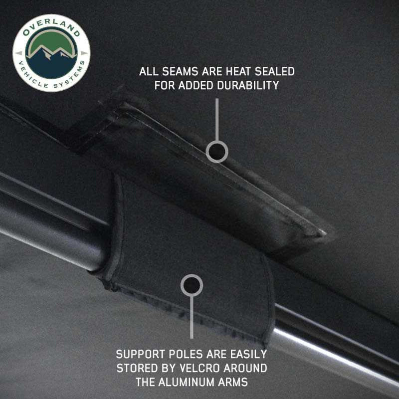 Image showing black Overland Vehicle Systems awning fabric with hanging loops to roll up and secure doors and windows. The awning is partially deployed, and the "Overland Vehicle Systems" logo is in the top left corner