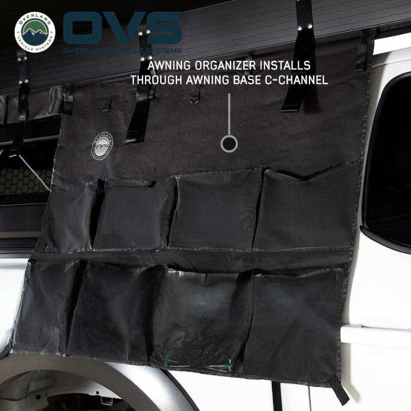 Image of an OVS XD Nomadic 270 LTE awning organizer mounted beneath the awning using the integrated C-channel, featuring multiple black storage pockets, shown on a vehicle in side view against a white background.