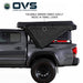 Image of an OVS XD Nomadic 270 LTE awning partially folded and packing into its travel cover on a pickup truck, black fabric shown mid-collapse in side view on a white background.