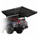 Image of an OVS XD Nomadic 270 LTE vehicle-mounted awning fully deployed from the rear of a pickup truck, black fabric with integrated LED lighting, shown in angled rear and side view on a white background.