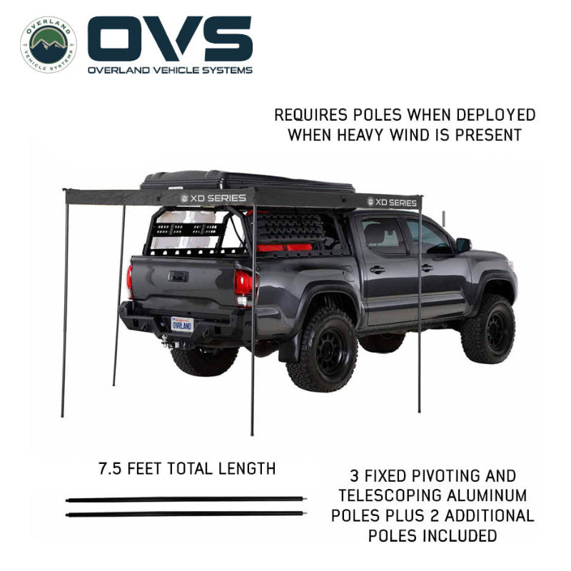 Image of an OVS XD Nomadic 270 LTE awning deployed on a pickup truck using aluminum support poles for stability in windy conditions, black fabric shown in angled rear and side view on a white background.