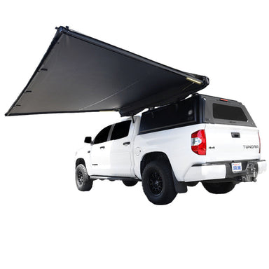 Image of OVS Nomadic 180 Awning partially deployed with LED lights, black fabric, angled rear and side view on white Toyota Tundra pickup truck on white background