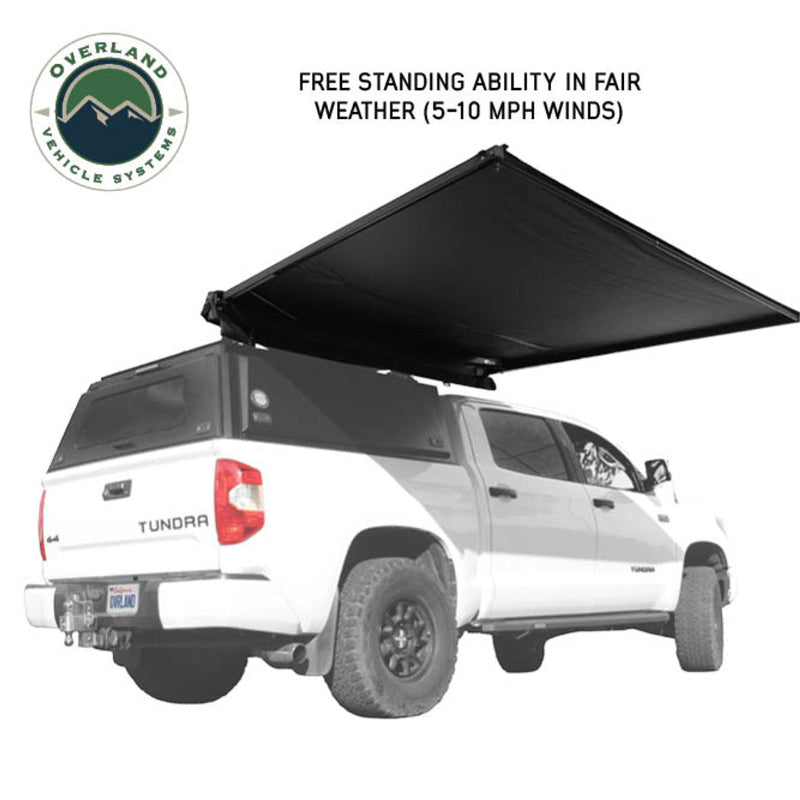 Image of the Nomadic 90 Awning fully deployed, showcasing its free-standing ability in fair weather. The awning has black fabric and is shown from an angled rear and side view on a white truck