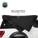 Side view of a white pickup truck with the OVS Nomadic Awning in the process of being stowed away. The black awning fabric is being collapsed, with an annotation explaining that the arms are being folded to prepare for closure