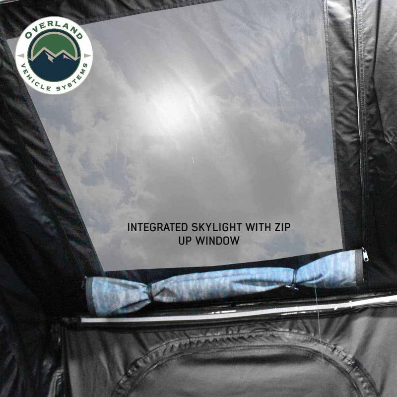 Image displaying the interior of a rooftop tent, highlighting an integrated skylight with a zip-up window, showing a cloudy sky through the clear panel. The "Overland Vehicle Systems" logo is in the top left corner