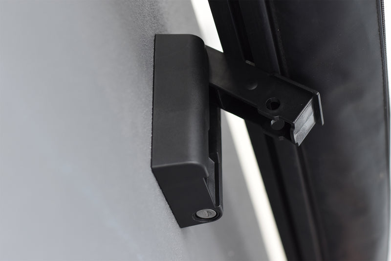 Image of a black RACKS BRAX HD Hitch component mounted on a dark surface, with a keyhole visible and another black bracket connecting it to a dark awning or roof rack component, viewed from an angled perspective.