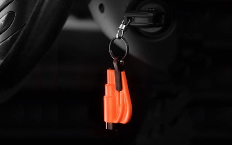Image, mostly dark, showing an orange Resqme tool dangling from a keychain in a car's ignition, with parts of the steering wheel visible in the foreground.