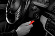 Image, mostly black and white, showing a hand holding a red Resqme tool attached to car keys in the ignition, with the car's steering wheel and dashboard visible.