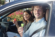 Image of a smiling man and woman in a car, both holding up Resqme keychain tools (the man holding a green one, the woman a red one), with flowers visible outside the car window.