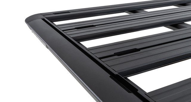 Image of Rhino-Rack roof rack, black aluminum frame with slatted design, close-up angled side view showing grooves and edges on white background