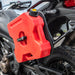 Image of RotopaX 1.75 Gallon Gasoline fuel container mounted on motorcycle side rack, red can with black mount and yellow cap insert, angled side view outdoors.