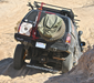 Image of off-road SUV driving on sandy terrain with rear-mounted RotopaX white water container, spare tire, and roof rack accessories, angled rear view in desert setting.