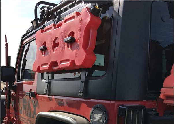 Red RotoPaX gasoline can with two black RotoPaX mounts, attached to the side window of a red Jeep, angled side view.