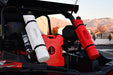 Three Rotopax fuel containers—one white 1.5-gallon, one red 2-gallon, and one red 1.5-gallon—are mounted on the back of an off-road vehicle with a scenic mountain range in the background.