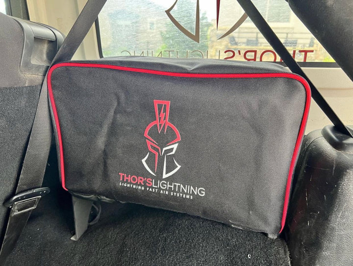 Image of Thors Lightning portable 12V air compressor protective cover in black with red trim secured in vehicle cargo area, angled front view inside SUV.
