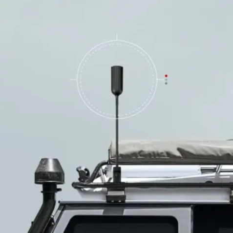 Image of a black cellular antenna mounted on the roof rack of a gray off-road vehicle, with a white, circular targeting reticle overlayed on the antenna. A white rooftop tent and a black snorkel are also visible on the vehicle